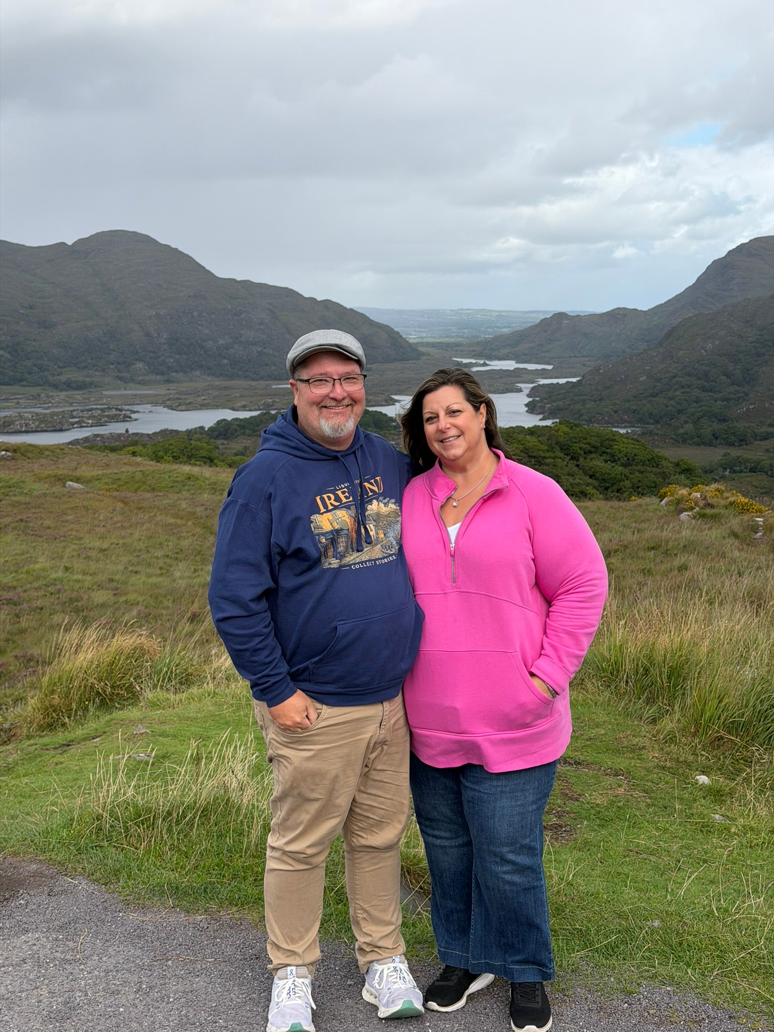 Rusty and Shelley overlooking the mountains and lakes in Ireland, with Rusty wearing a Liquid Itinerary hoodie.